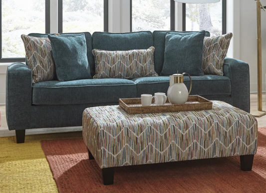 A teal sofa with a multicolored geometric pattern, placed in a bright living room setting.