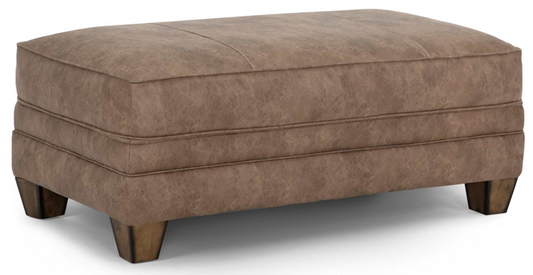 A large, overstuffed brown faux leather ottoman with solid wooden legs and padded roll arms.