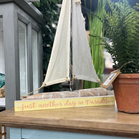 Decorative sailboat on a wooden surface with a sign reading 'just another day in Paradise'.