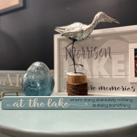 Decorative sign with text 'at the lake where doing absolutely nothing is doing something' on a surface.