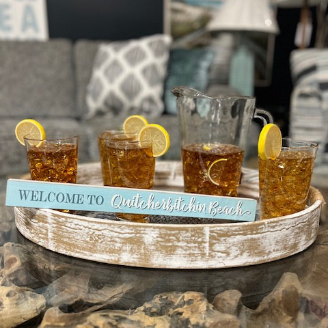 Tray with glasses of iced tea and a pitcher, featuring a decorative sign, on a stone surface.