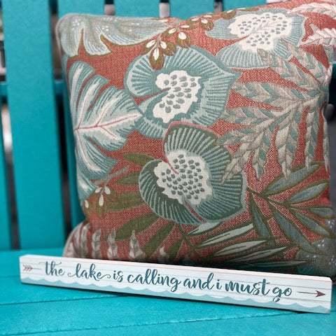 Decorative pillow with floral pattern on a teal chair, accompanied by a wooden sign.