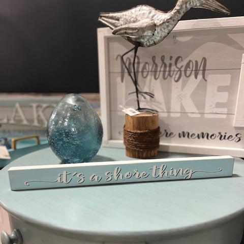 Decorative sign with 'it's a shore thing' on a table with decorative items.