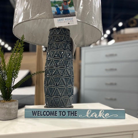 Decorative lamp with textured design on a surface, featuring a 'Welcome to the Lake' sign.