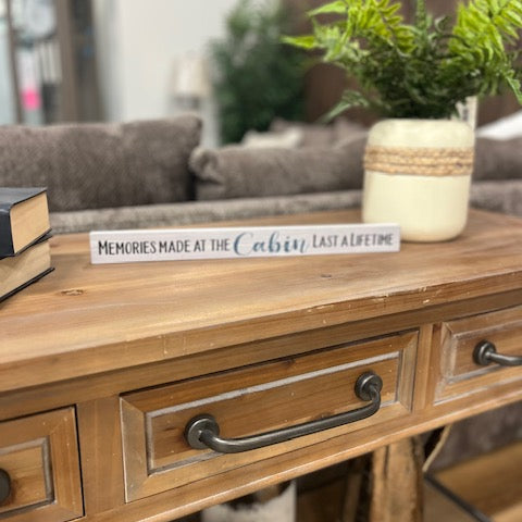 Wooden console table with decorative items including a book, plant, and sign in a living room setting.