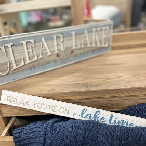 Decorative sign with 'Relax, you're on lake time' text on a wooden surface.