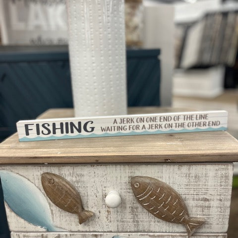 Decorative sign with fishing-themed text on a wooden surface with fish designs.