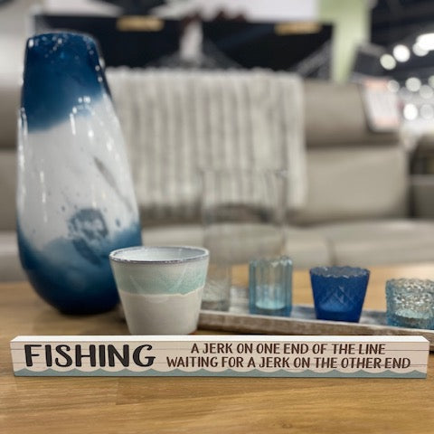 Wooden block with fishing joke on a table with decorative items in the background