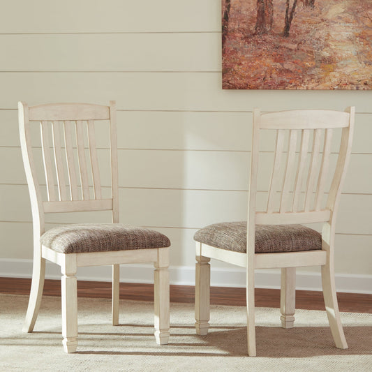 Two wooden chairs with patterned cushions on a carpeted floor, with a painting on the wall in the background.
