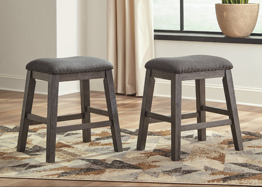 Two gray stools on a patterned rug with a neutral-colored wall and plant in the background.