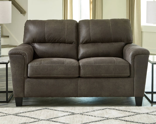 gray leather loveseat in a living room setting with a rug and lamp visible.
