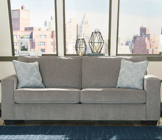 Gray sofa with decorative pillows in a room with large windows showing a cityscape.