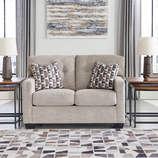 Beige loveseat with patterned cushions in a living room setting with tables and decor.