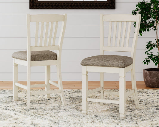 Two white chairs with gray cushions on a rug in a room with a plant and framed picture.