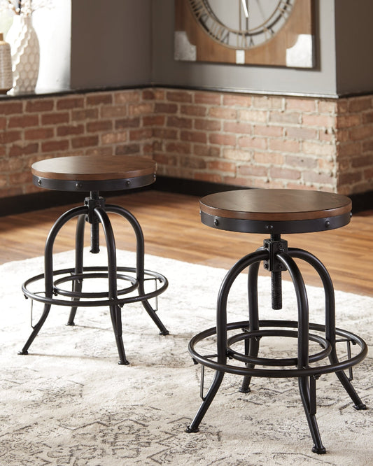 Two wooden stools with metal legs on a textured rug in a room with brick walls.