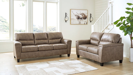 Brown leather sofa set in a living room with large windows and a plant.