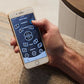 Hand holding a smartphone with a chair control app on a carpeted floor.