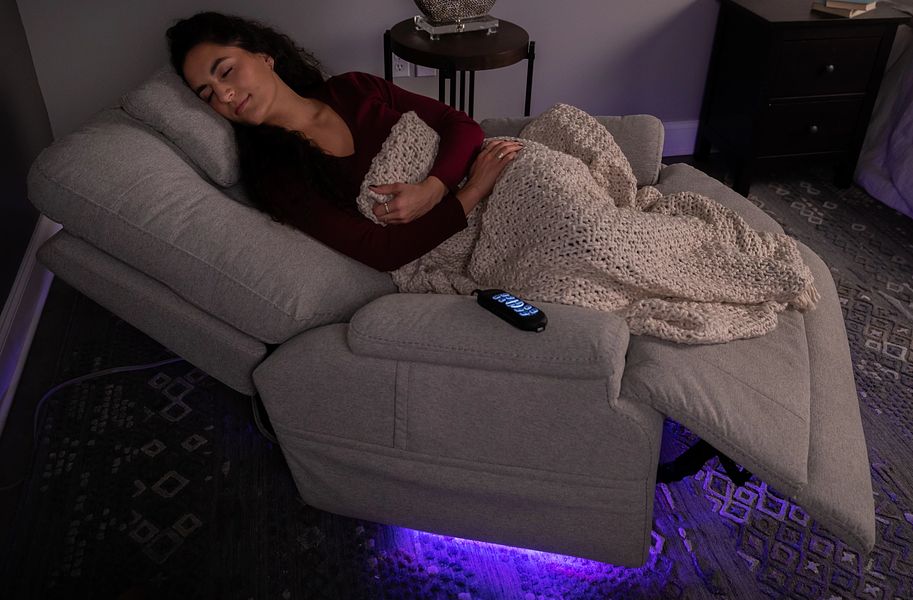 Woman lying on a gray sofa with a blanket, surrounded by dim lighting.
