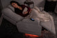 Woman lying on a gray recliner with a blanket, surrounded by dim lighting.