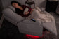 Woman relaxing on a gray recliner with a blanket, surrounded by dim lighting.