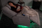 Woman sleeping on a gray recliner with a blanket and remote control in a dimly lit room.