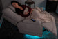 Woman lying on a gray couch with a blanket, surrounded by dim lighting.