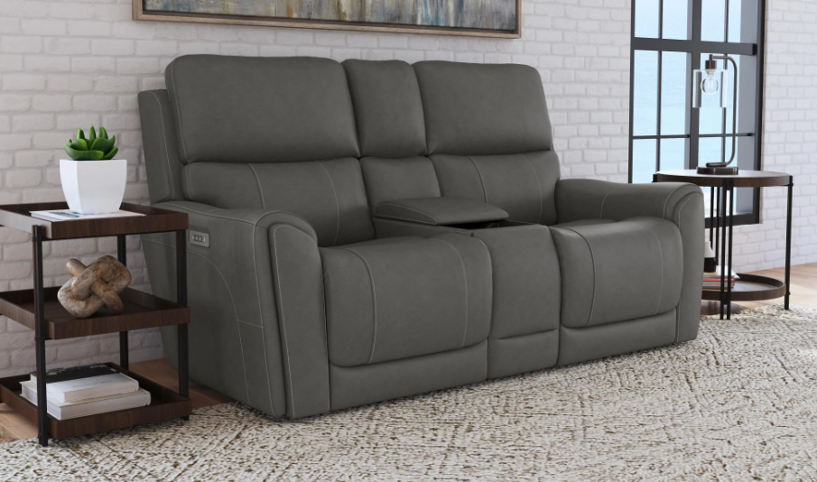 Gray sectional sofa in a living room setting with a brick wall and small table.