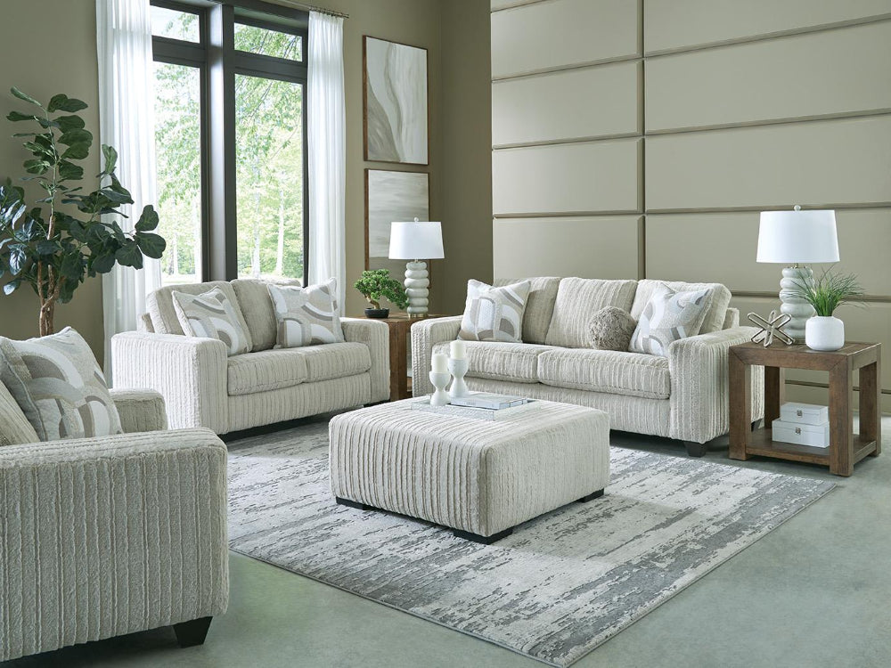 Living room with beige sofa, armchair, and ottoman on a patterned rug.