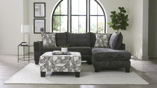 Gray sectional sofa with patterned ottoman in a living room setting.