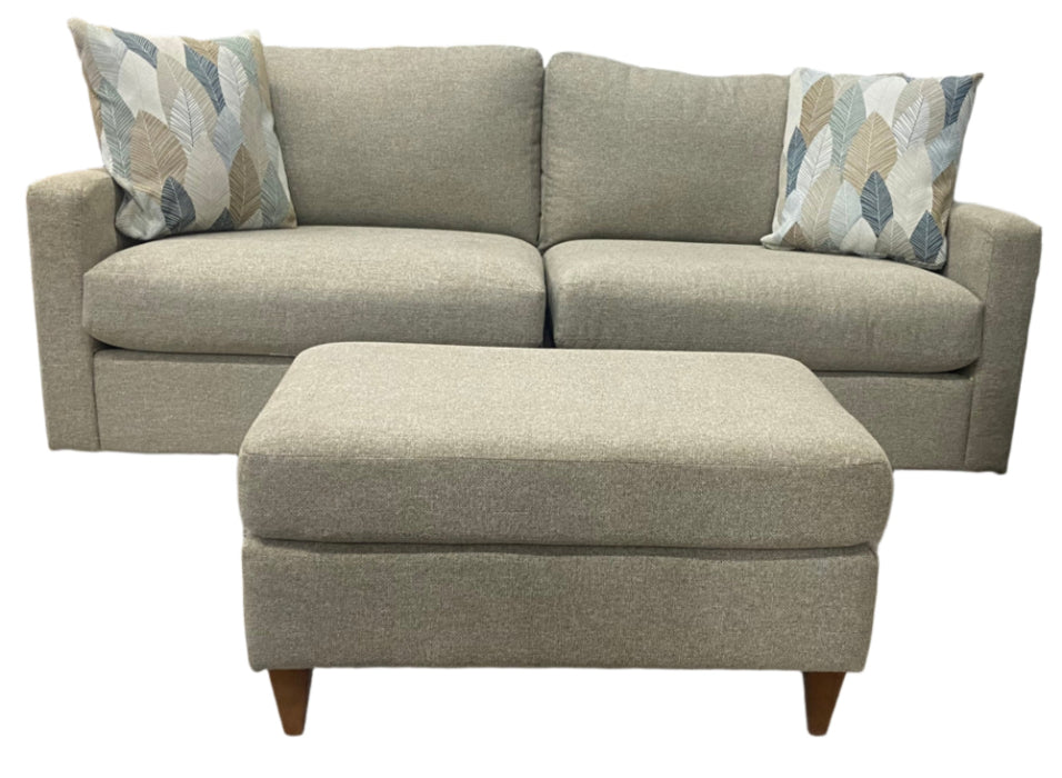 Beige sofa with two patterned cushions with matching ottoman on a white background
