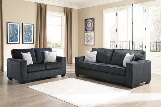 Gray sofa set in a living room with large windows and curtains.