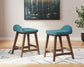 2 teal upholstered stools on a white rug with an abstract painting on the wall