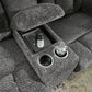 Gray textured loveseat with cup holder and tray containing a phone, glasses, and a glass of water.