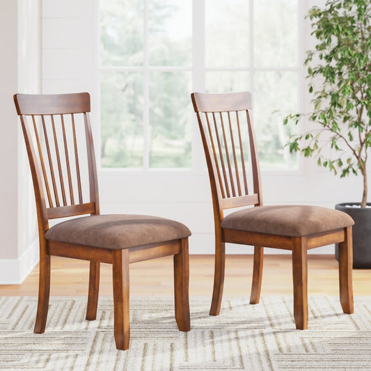 Two wooden chairs with brown cushioned seats in a room with a plant and window.