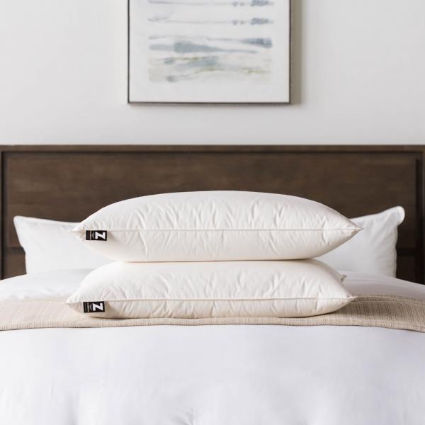 Stack of pillows on a neatly made bed with a headboard and artwork in the background.