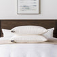 Stack of pillows on a neatly made bed with a headboard and artwork in the background.
